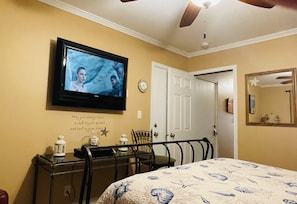 A bedroom with a bed, a television on the wall, a desk with a chair, and a door.