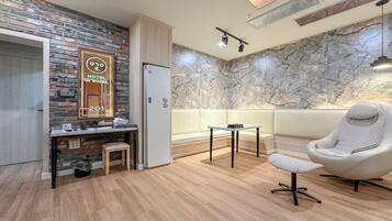 Une chambre d’hôtel avec un plancher en bois, un mur en marbre, un fauteuil blanc, une petite table et un bureau avec un miroir.
