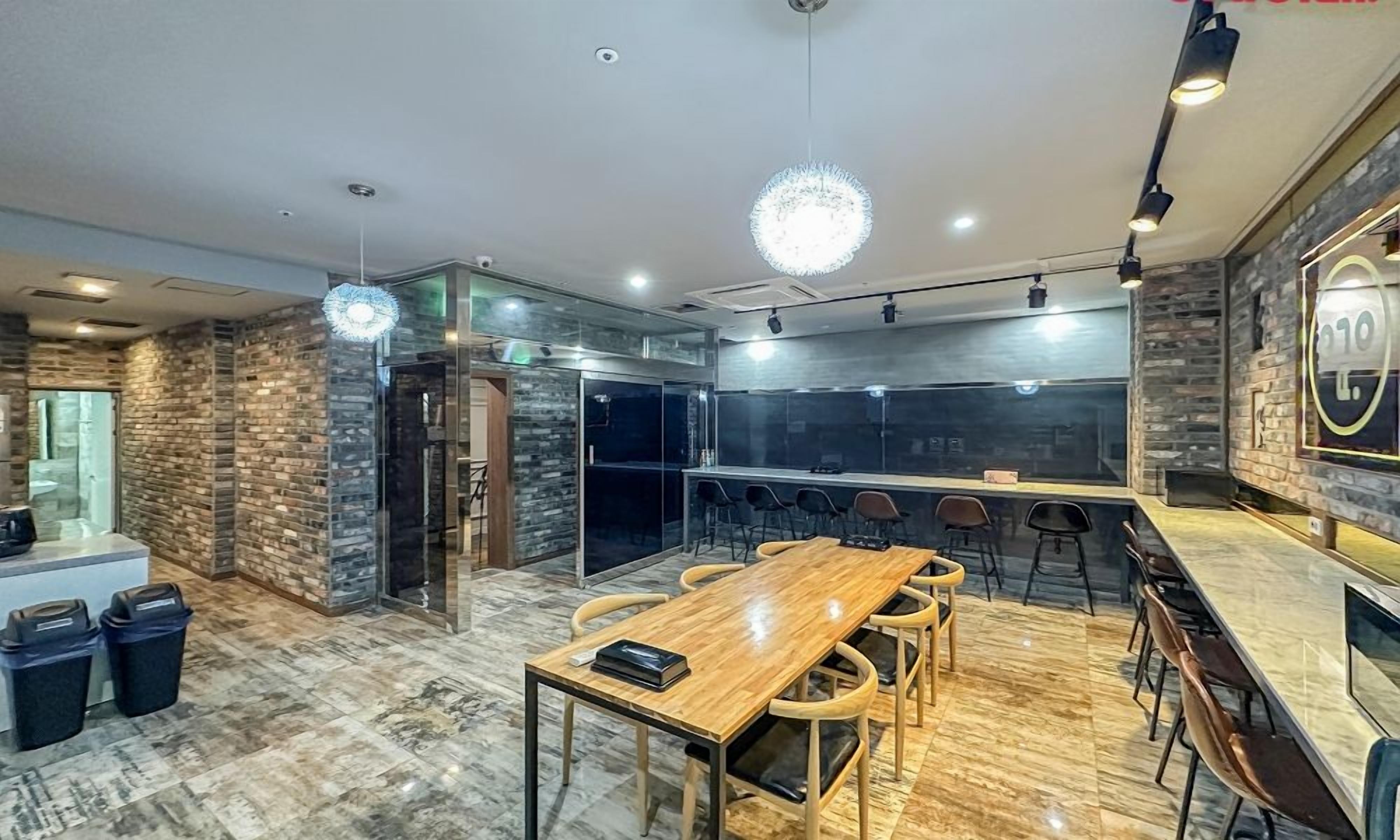 A modern kitchen with a wooden table and chairs, a hanging light fixture, and a brick wall.