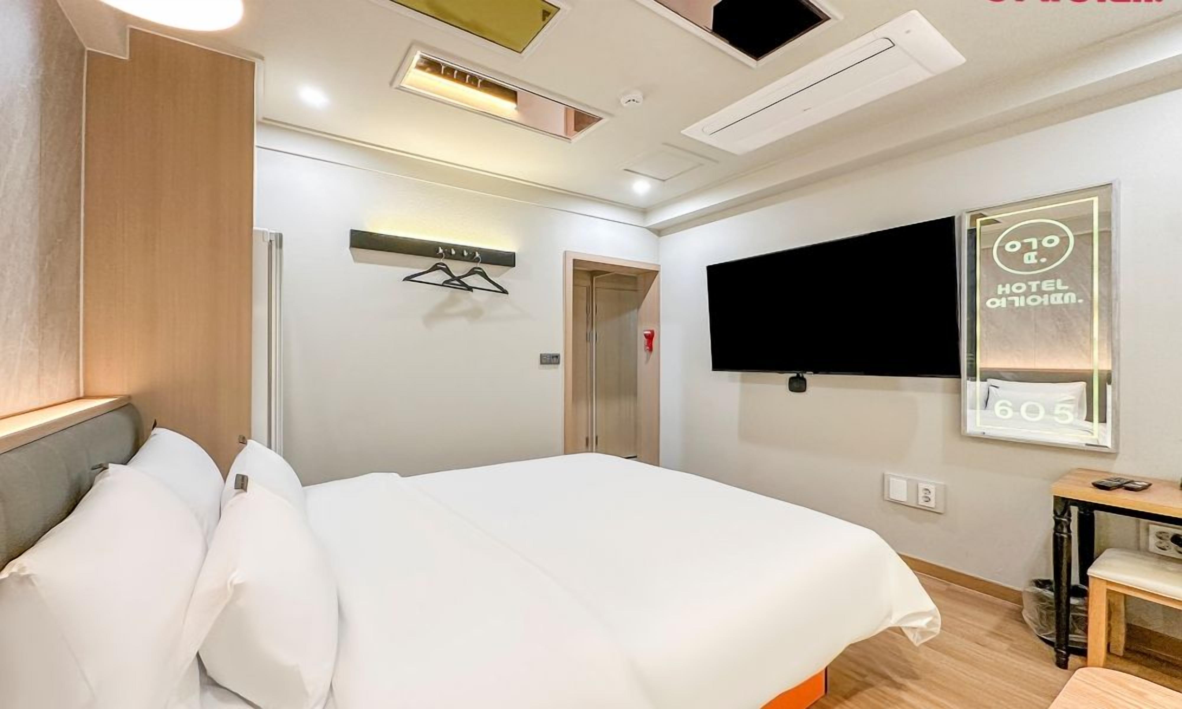 A hotel room with a bed, a TV mounted on the wall, a wooden headboard, and a small table.