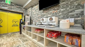 A hotel reception area with a brick wall, a flat-screen TV mounted above the counter, and shelves stocked with snacks.