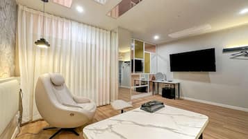 A modern hotel room with a massage chair, a flat-screen TV, a marble-topped table, and a large mirror.