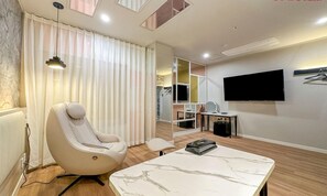 Una habitación de hotel moderna con sillón de masajes, televisor de pantalla plana, mesita de mármol y un espejo grande.