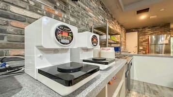 A kitchen with two coffee machines on a granite countertop, a brick wall, and a stainless steel refrigerator in the background.