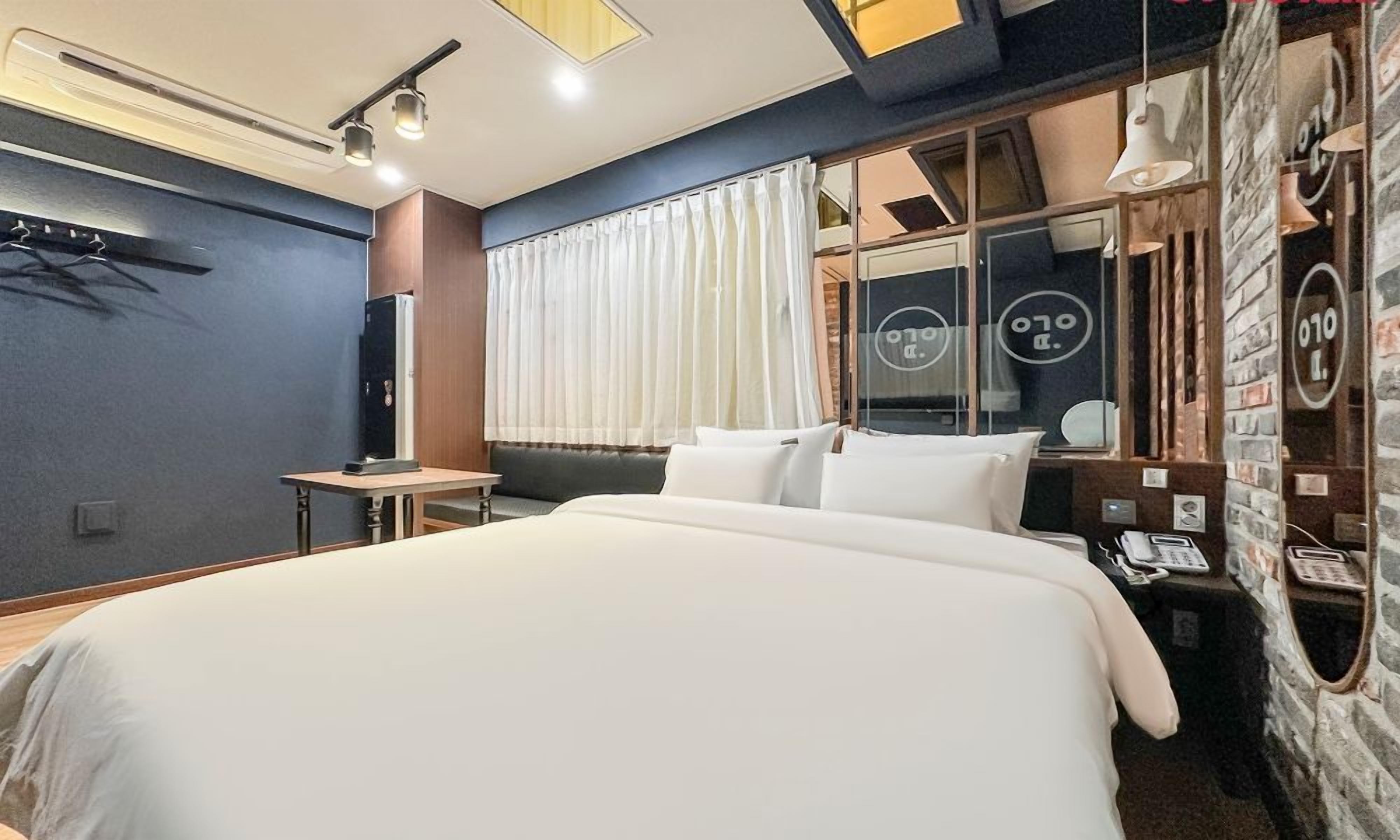 Habitación de hotel moderna con una cama grande, un escritorio, un teléfono y un ventanal con cortinas.