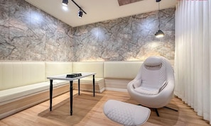 Habitación moderna con pared de mármol, un banco acolchado blanco, una silla blanca, una mesita y una lámpara colgante.