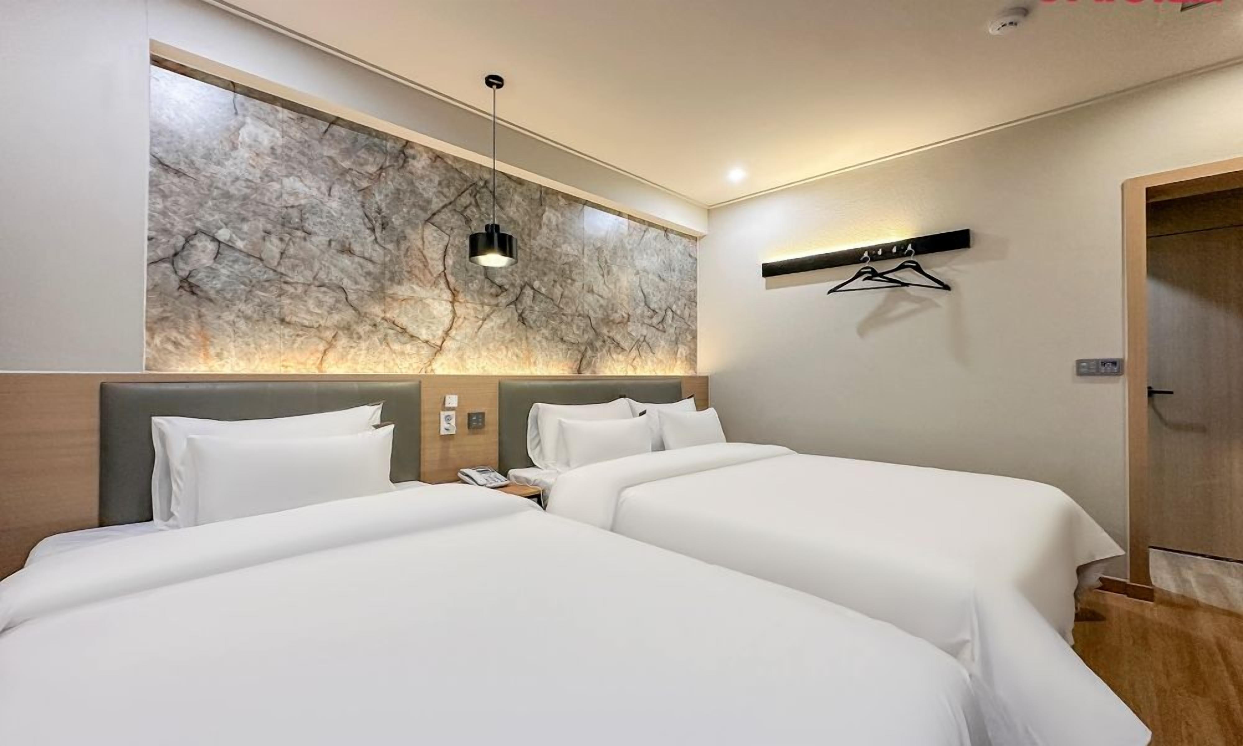 Habitación de hotel con dos camas, una pared de mármol, una lámpara colgante y un perchero.