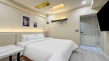 A hotel room with a large bed, a bedside table, a wall-mounted TV, and a door leading to another room.