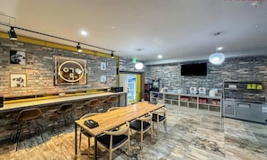 Un área de bar moderna con mostrador de madera, taburetes y pared de ladrillo de fondo.