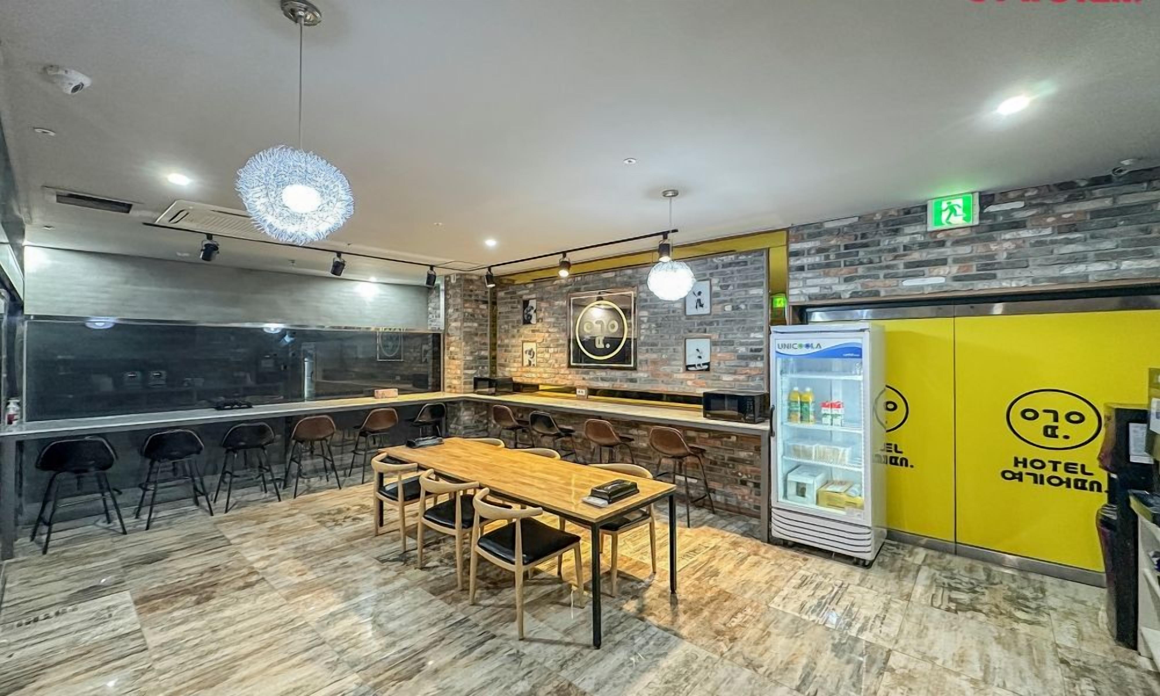 A modern hotel lobby with a bar area, seating arrangements, and a refrigerator stocked with beverages.