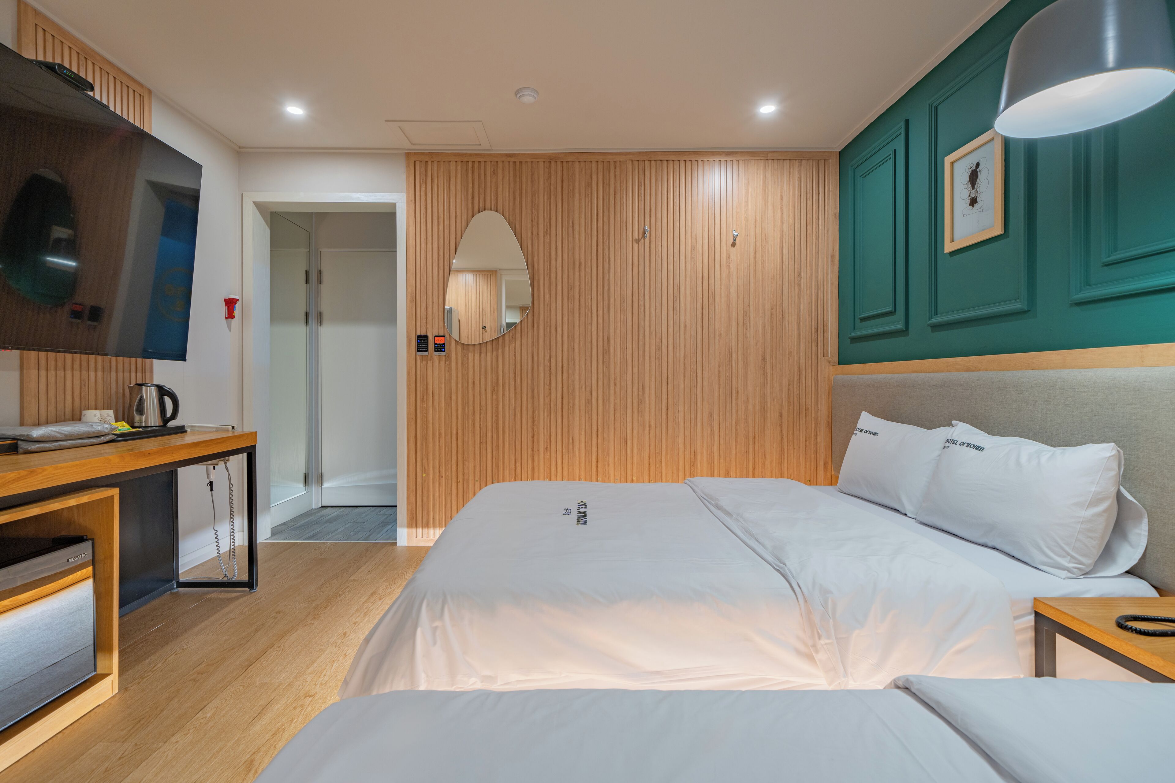 A modern hotel room with a large bed, a desk with a flat-screen TV, a mirror, and wooden paneling on the walls.