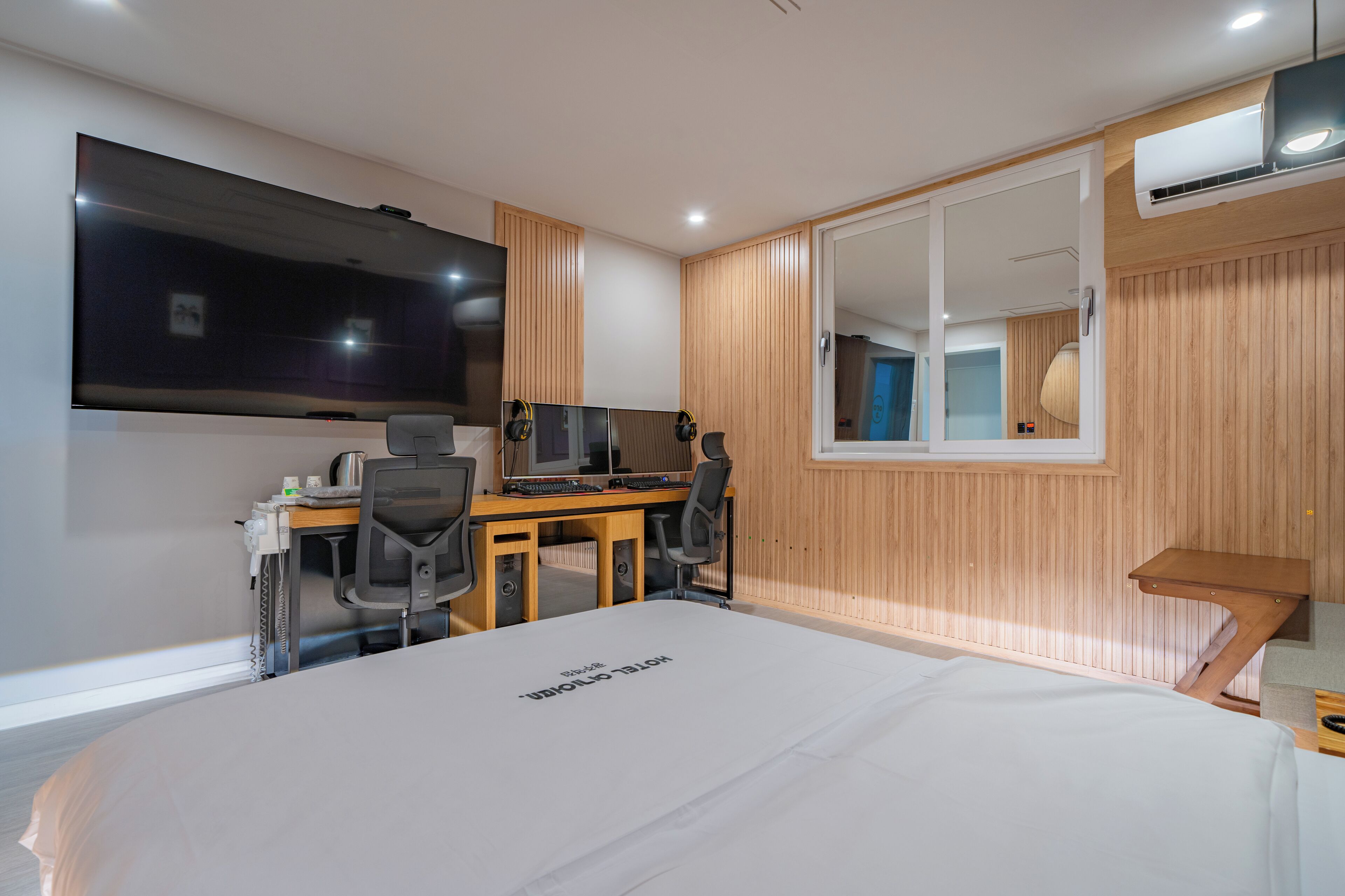 A modern hotel room with a large bed, a desk with a computer, a TV, and a large mirror.