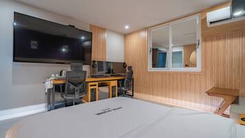 A modern hotel room with a large bed, a desk with a computer, a TV, and a large mirror.