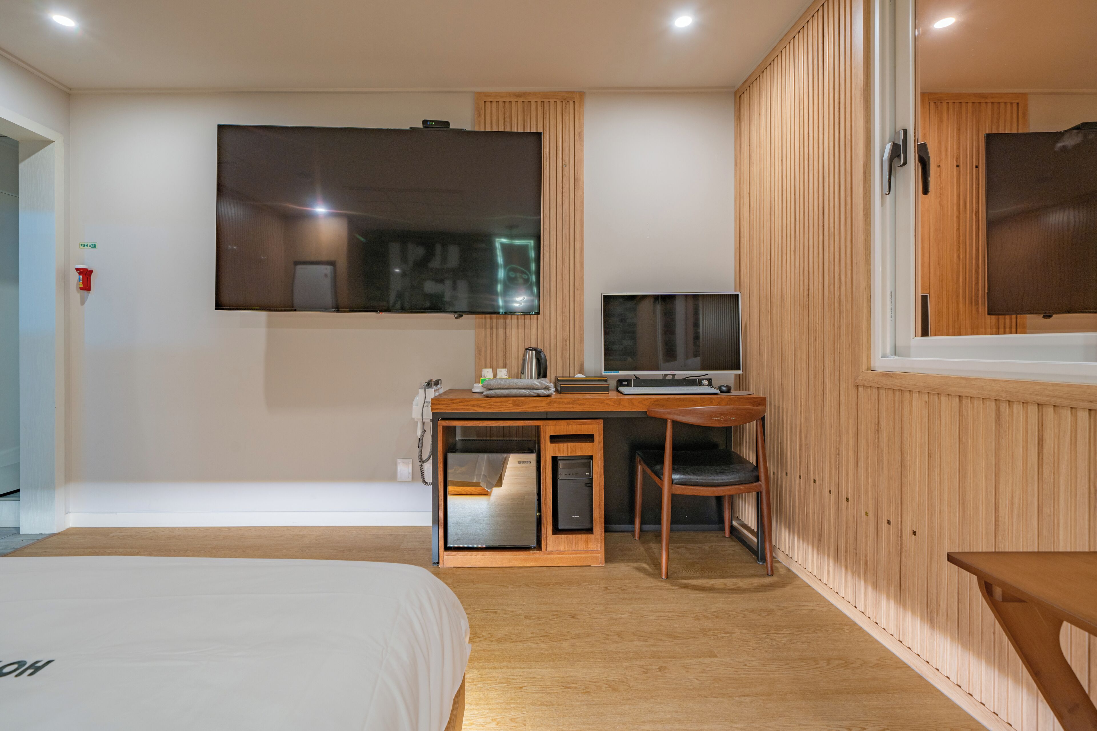 Una habitación de hotel moderna con una cama, un escritorio con una computadora, un televisor y un panel de pared de madera.