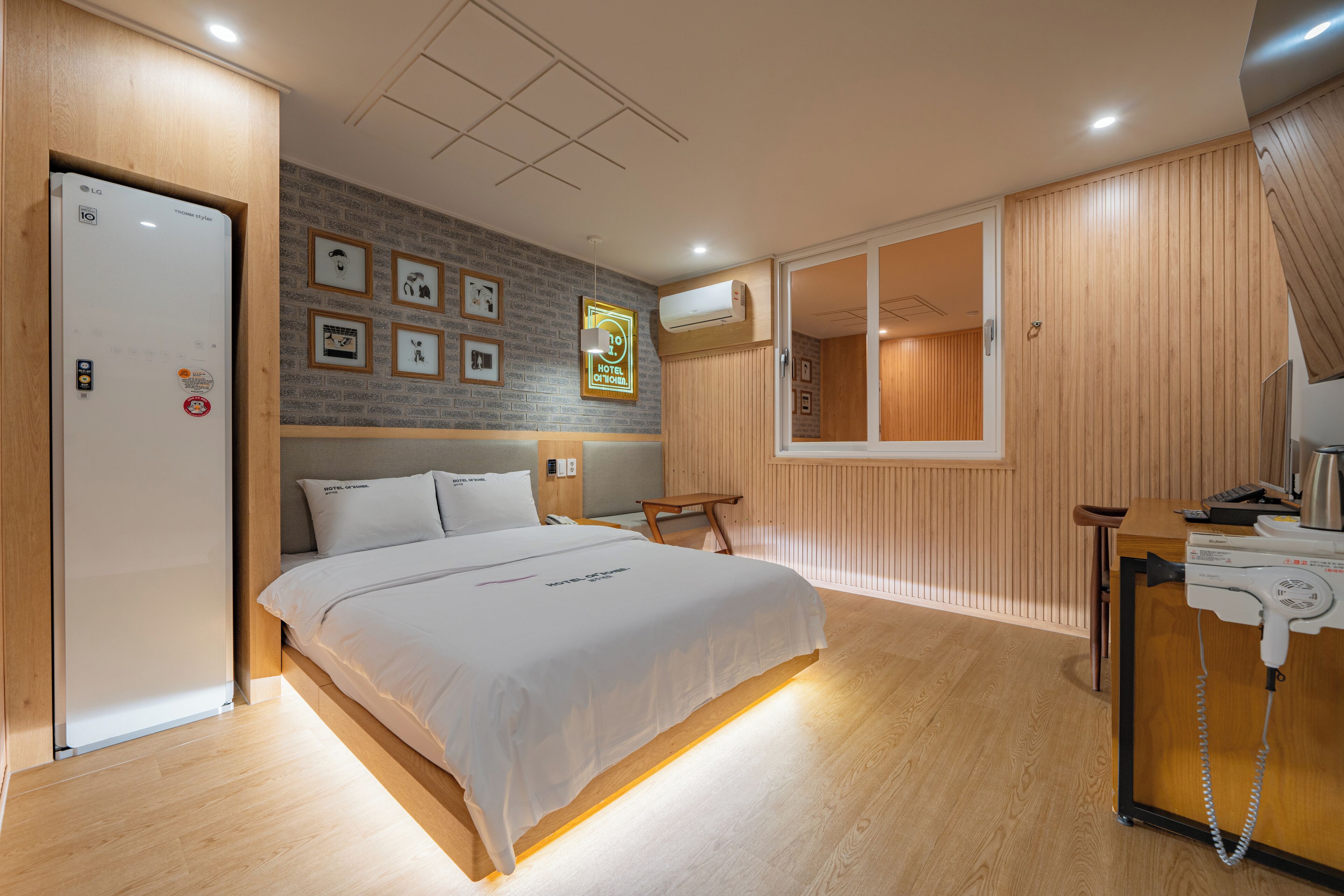 A modern hotel room with a large bed, wooden paneling, a desk with a phone, and framed pictures on the wall.