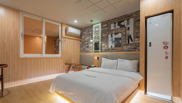 Habitación de hotel con cama, piso de madera, pared de ladrillo y puerta blanca.