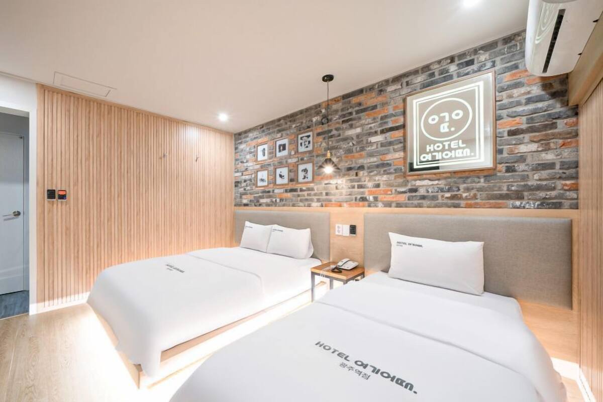 Habitación de hotel con dos camas, un panel de pared de madera, una pared de ladrillo con cuadros enmarcados y un letrero que dice "HOTEL CITY OMM".