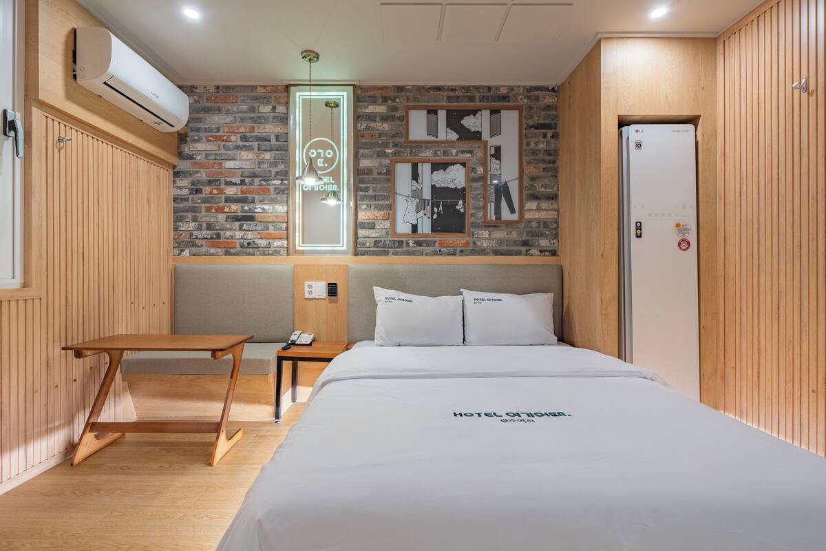 Una habitación de hotel con una cama, una mesita de noche de madera, un aire acondicionado instalado en la pared y una puerta con cerradura.