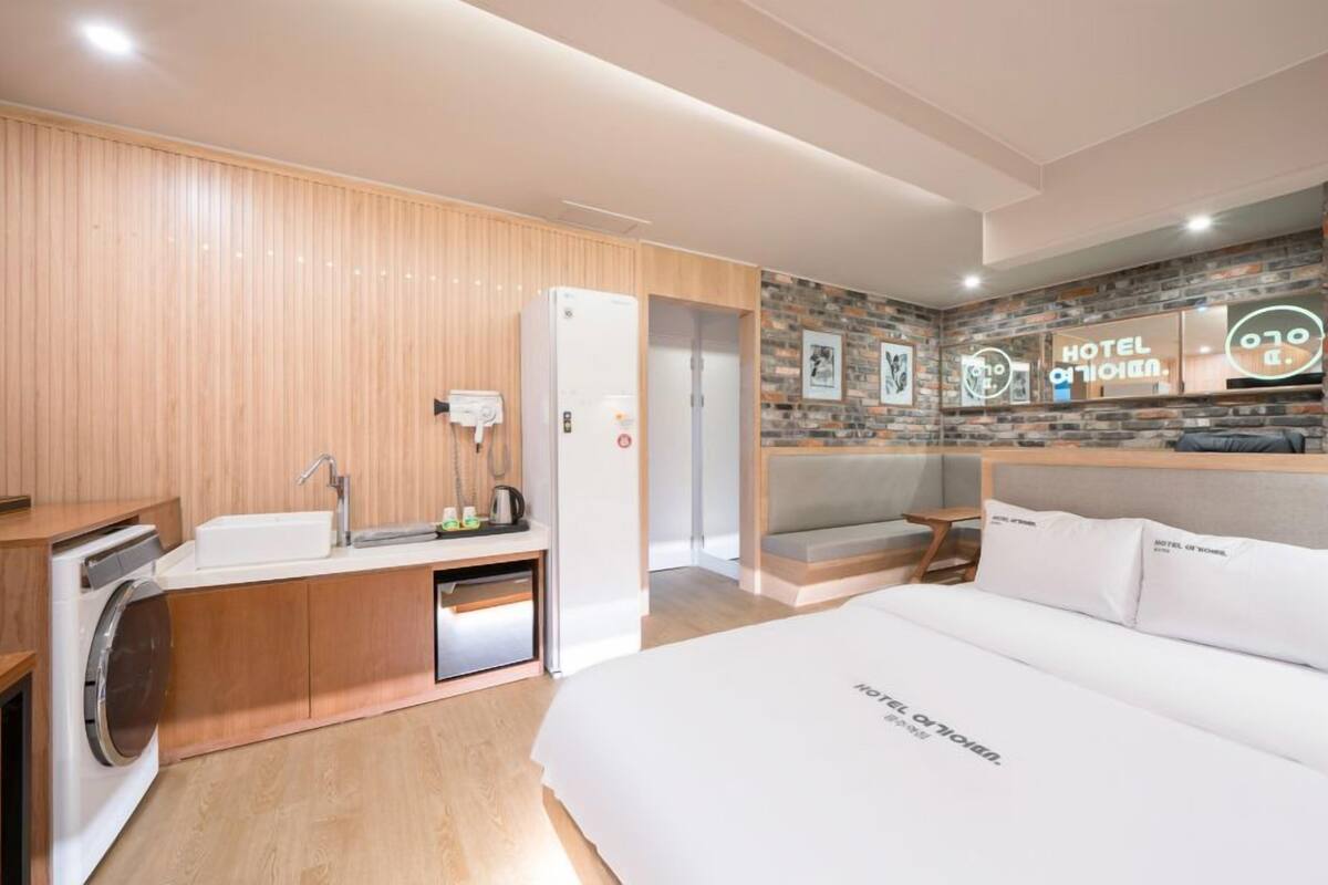 Habitación de hotel con pared de paneles de madera, un escritorio empotrado con lavamanos, cama con ropa blanca y pared de ladrillo con un cartel que dice 'HOTEL'.