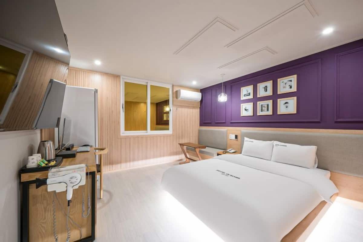 Una habitación de hotel moderna con una cama grande, un escritorio con computadora, una silla y una ventana.