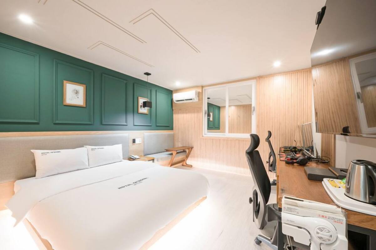 Una habitación de hotel con una cama, un escritorio con hervidor, una silla y un espejo.