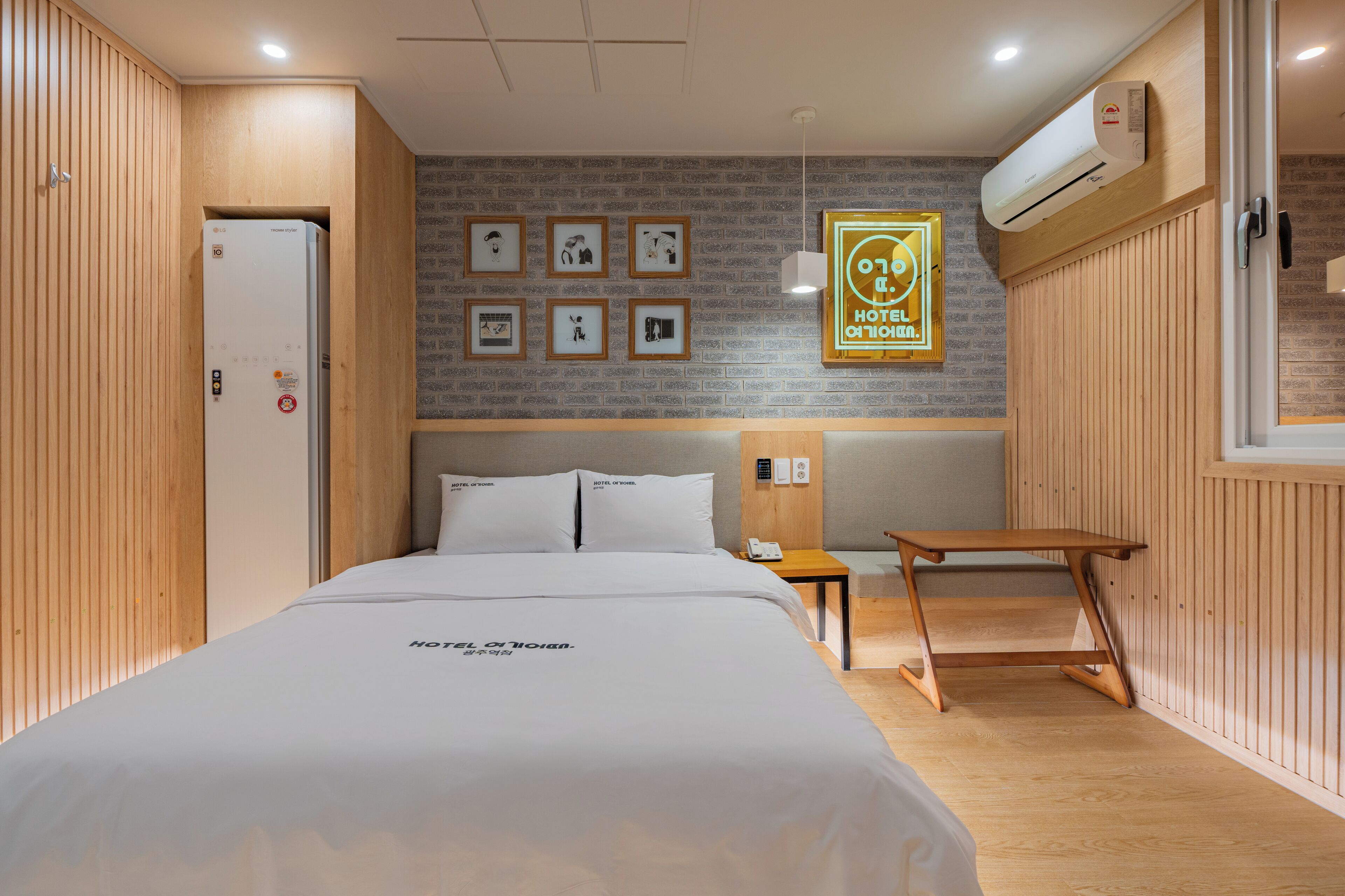 Una camera d'albergo con un letto, un tavolo di legno, un condizionatore d'aria a parete e quadri appesi alla parete.