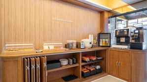 Zona de desayuno autoservicio con mostrador de madera, máquinas de café y alacenas.