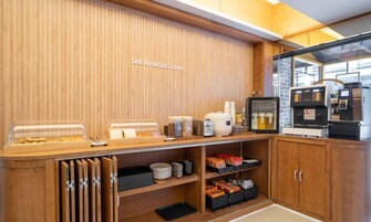 A self-service breakfast area with a wooden counter, coffee machines, and storage cabinets.
