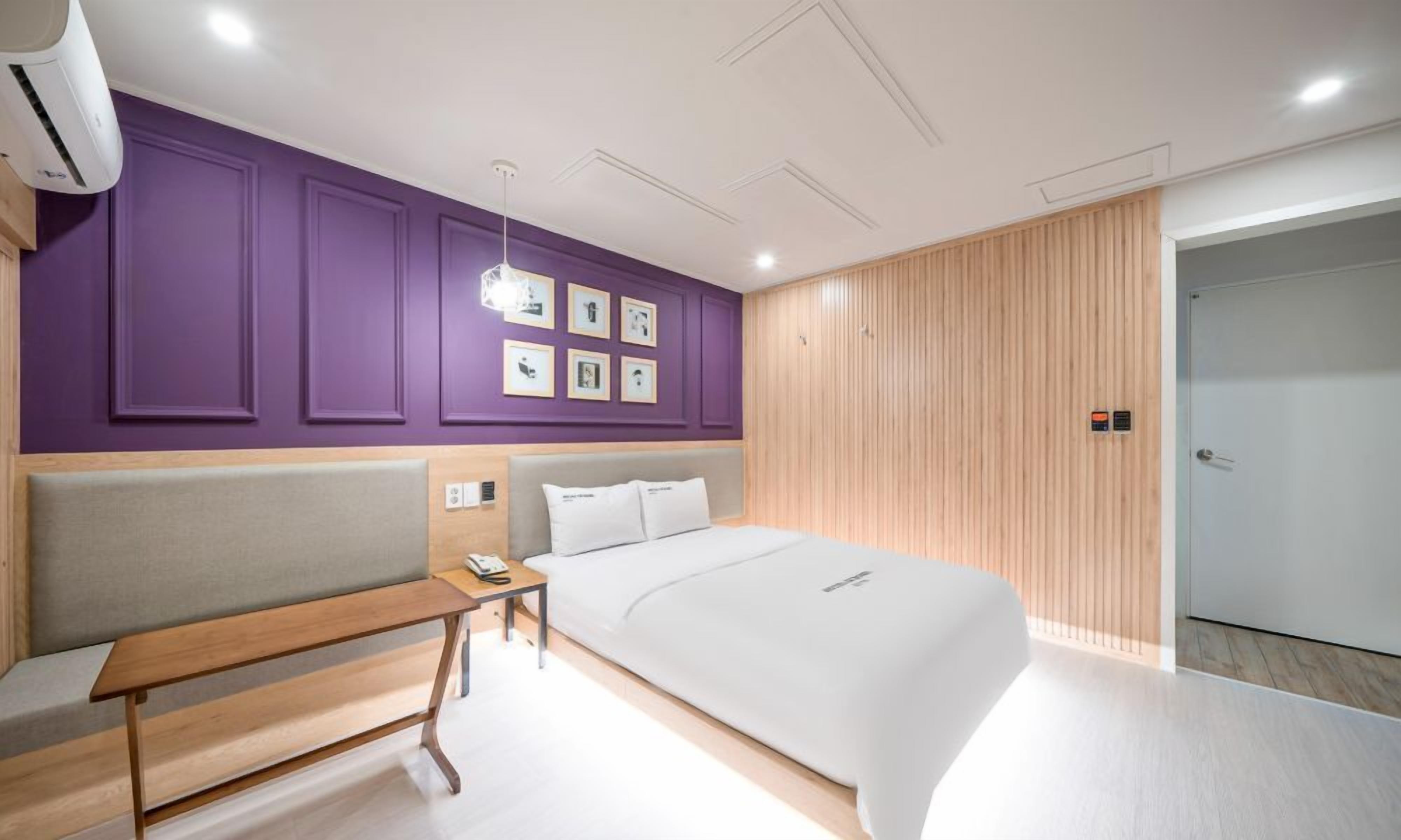 A modern hotel room with a large bed, a bedside table, a bench, and a wall with framed pictures.