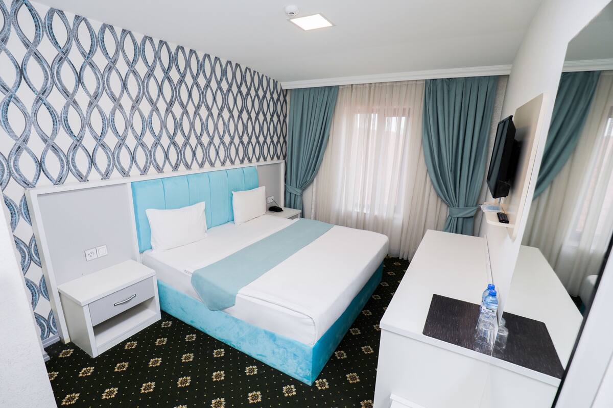 Une chambre d’hôtel avec un lit, des tables de chevet, un bureau, une télévision et des rideaux.
