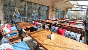 An outdoor seating area with wooden tables and chairs, some with striped cushions. -  Altus Hotel Baku - Free Massage (Baku)