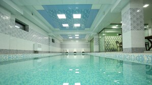 A large indoor swimming pool with a tiled floor and walls, a ceiling with recessed lighting, and a seating area with chairs and a table. -  Altus Hotel Baku - Free Massage (Baku)