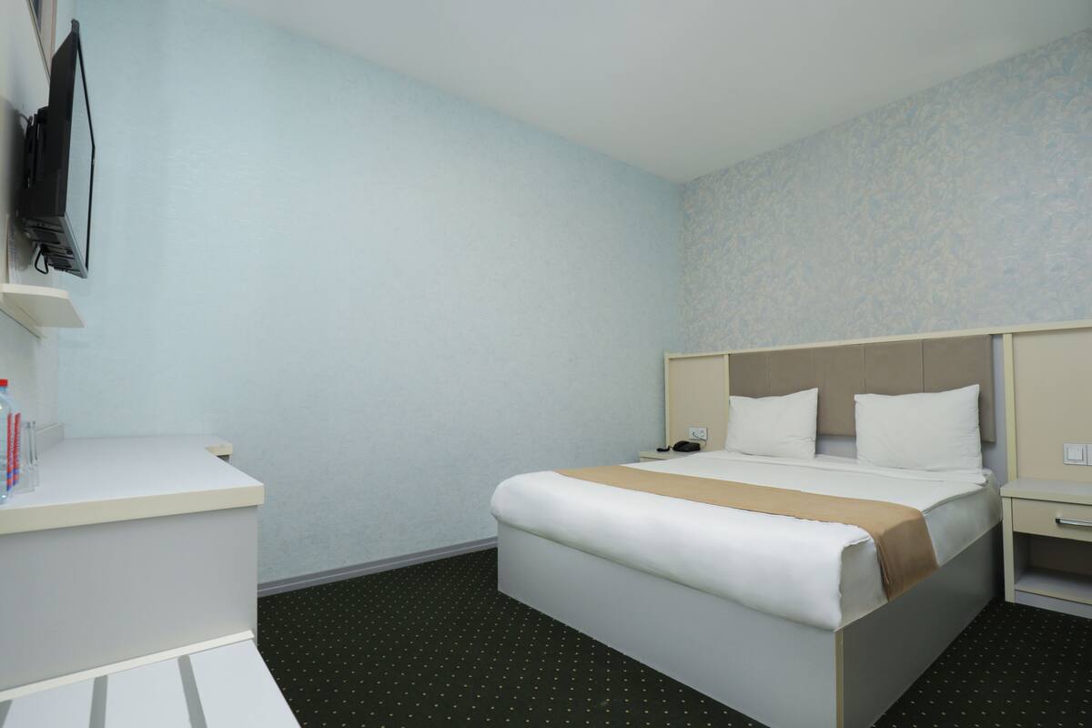 Une chambre d’hôtel équipée d’un lit, d’une table de chevet et d’un téléviseur fixé au mur.