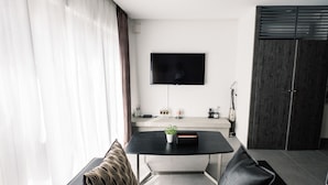 A modern living room with a flat-screen TV mounted on the wall, a dining table with a plant, and a dark wooden wardrobe. - Spatium Ginza (Tokyo)