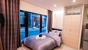 A modern bedroom with a large window, a bed with a headboard, a wardrobe, and a small table with towels. - Spatium Ginza (Tokyo)