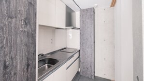 A modern kitchen with white cabinets, a stainless steel sink, and a wooden accent wall. - Spatium Ginza (Tokyo)
