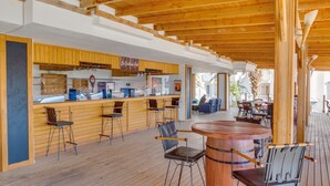 Une terrasse en bois avec un coin bar, des tabourets de bar et une table ronde en bois.