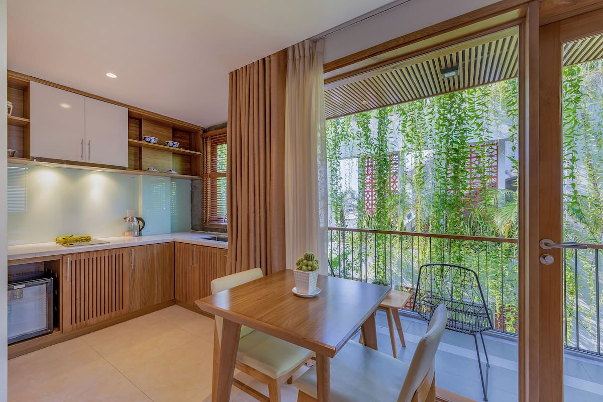 A modern kitchen with wooden cabinets, a dining table, and a balcony with a view of greenery.