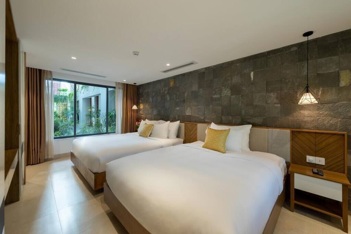 A hotel room with two beds, a large window, and a stone wall.