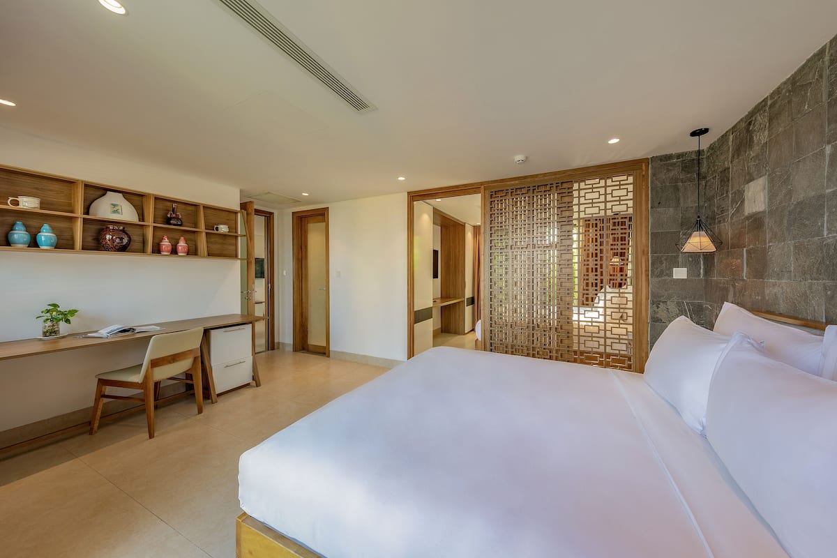 A bedroom with a bed, a desk, and shelves with decorative items.