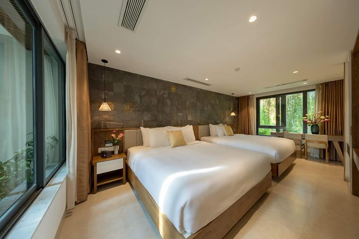 A modern hotel room with two large beds, a large window, and a stone accent wall.