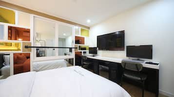 A hotel room with a bed, desk, chair, television, and wardrobe.