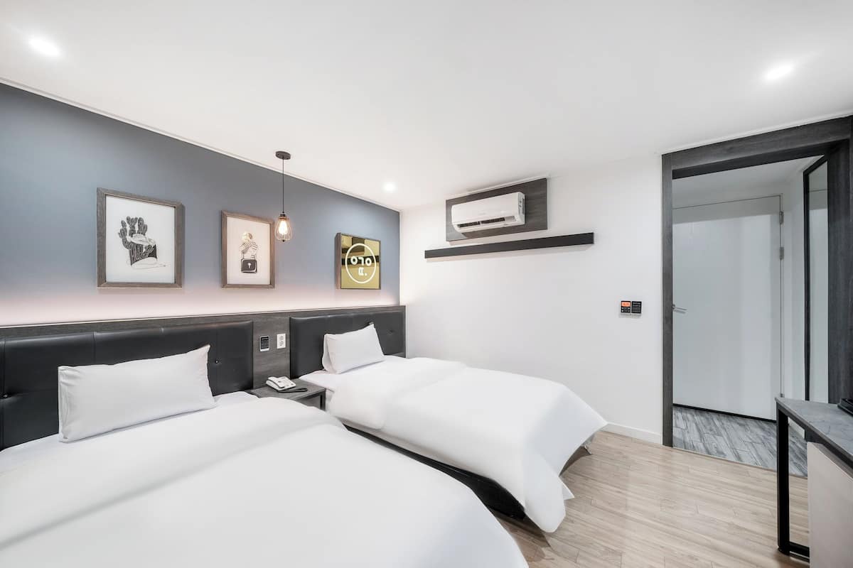 A hotel room with two beds, a desk, and a wall-mounted air conditioner.