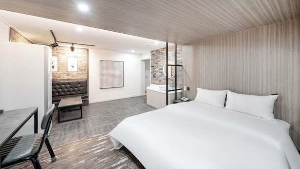 A modern hotel room with a large bed, a seating area with a sofa and table, a bathroom with a glass shower, and a brick accent wall. - HOTEL Yeogiuhtte Gwangju Baek Un (Gwangju)