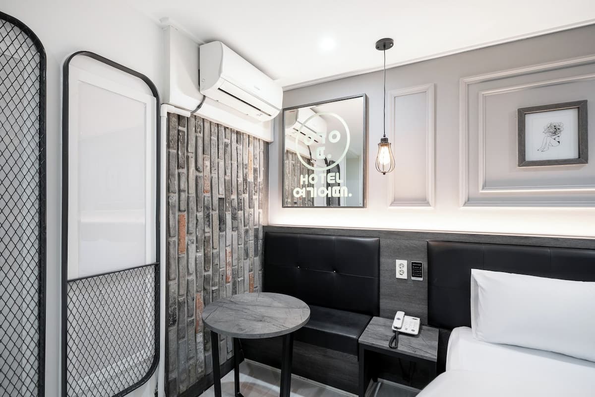 A modern hotel room with a black leather sofa, a small round table, a bed with white linens, and a wall-mounted air conditioner.