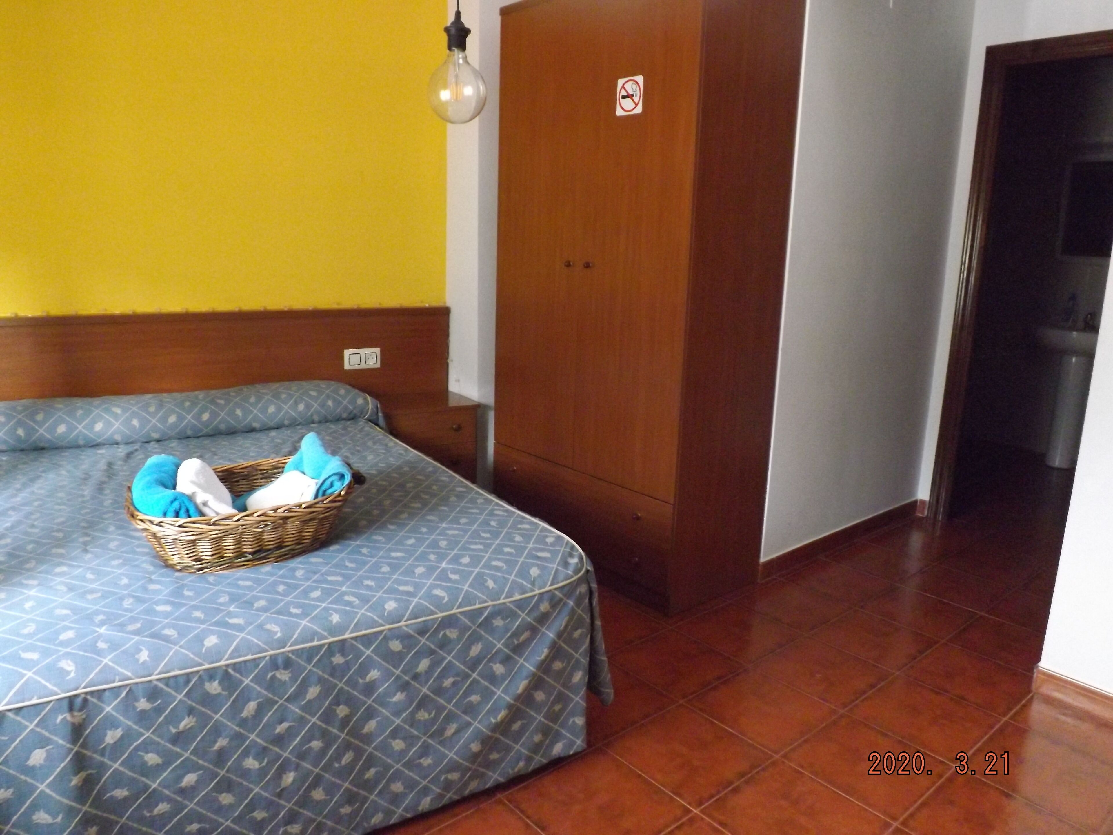 A room with a bed, a wooden wardrobe, a basket with clothes, and a light fixture.