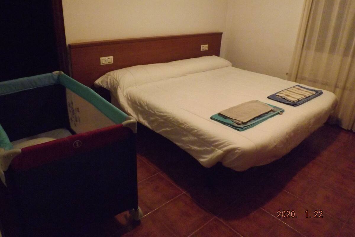Ein kleines Zimmer mit einem Einzelbett, einem Holzkopfstück, einem kleinen Nachttisch und einem roten Sessel.