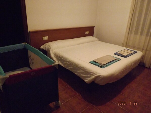 A small, single-bed room with a wooden headboard, a small bedside table, and a red chair.
