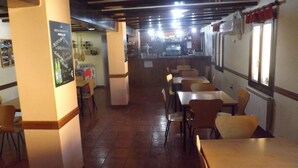 L’intérieur d’un restaurant avec des tables et des chaises en bois, un bar à l’arrière-plan et un menu écrit à la craie sur le mur.