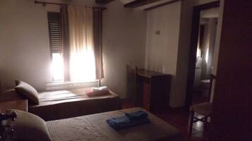 A small, dimly lit room with two beds, a chair, and a desk.